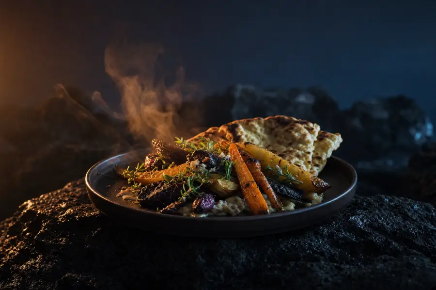 A hot festival meal of roasted vegetables, herbs and flatbread on a dark plate.